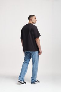 Black oversized T-shirt, short sleeves, rounded neckline; paired with light blue loose-fit jeans and black-and-white sneakers.