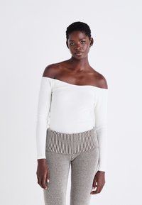 Off-shoulder vit ribbad långärmad topp kombinerad med beige och bruna randiga ribbade byxor, med ett brett midjeband.