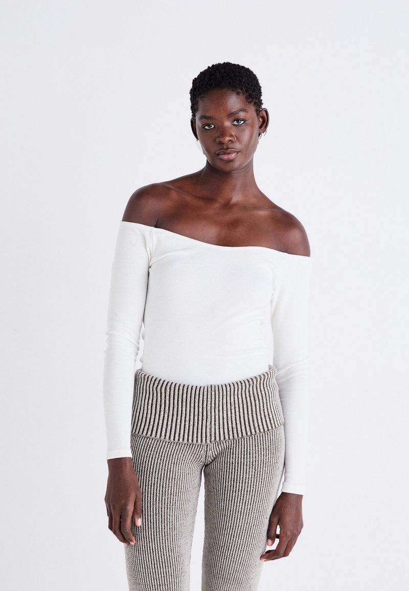 Off-shoulder vit ribbad långärmad topp kombinerad med beige och bruna randiga ribbade byxor, med ett brett midjeband.