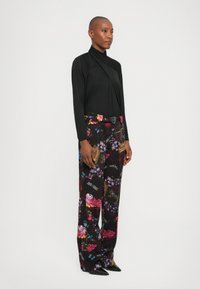 Zwarte lange mouw top met een kruisontwerp, gecombineerd met loszittende, gestreepte broeken in zwart, paars en roze met bloem- en abstracte motieven.