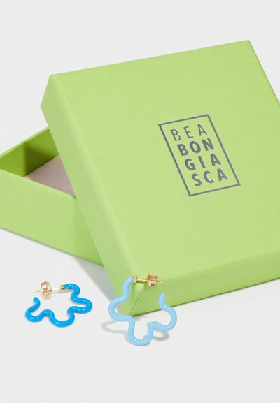 Μπλε και ανοιχτόμπλε σκουλαρίκια σε σχήμα σύννεφου με χρυσή βάση, παρουσιασμένα σε πράσινο κουτί με λογότυπο στο καπάκι.