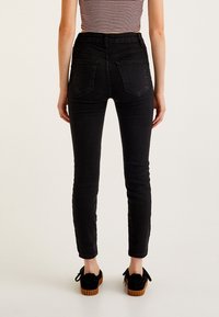 Jeans skinny negros de cintura alta con una textura suave, que cuentan con dos bolsillos traseros y una silueta ajustada, combinados con zapatos de plataforma negros.