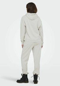 Helle graue Kapuzenjacke und Jogginghose aus weichem Material, mit lockerem Schnitt. Kombiniert mit schwarzen Schnürboots mit metallischen Akzenten.