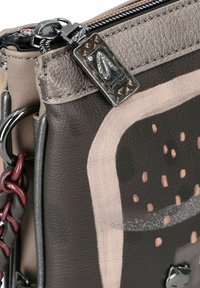 Primer plano de un bolso de cuero marrón y beige con cremallera, etiqueta de logo metálico y detalle de asa de cuero trenzado.