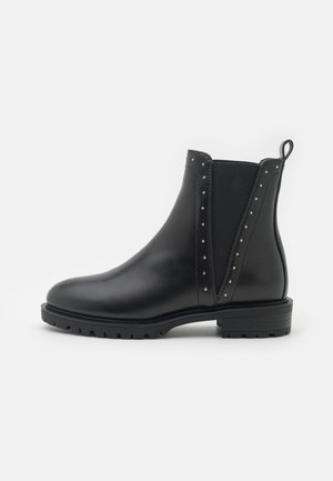 Bottines en cuir noir avec des panneaux élastiques sur les côtés, des accents cloutés, un bout arrondi et une semelle en caoutchouc texturé. Comprend une languette au niveau du talon.