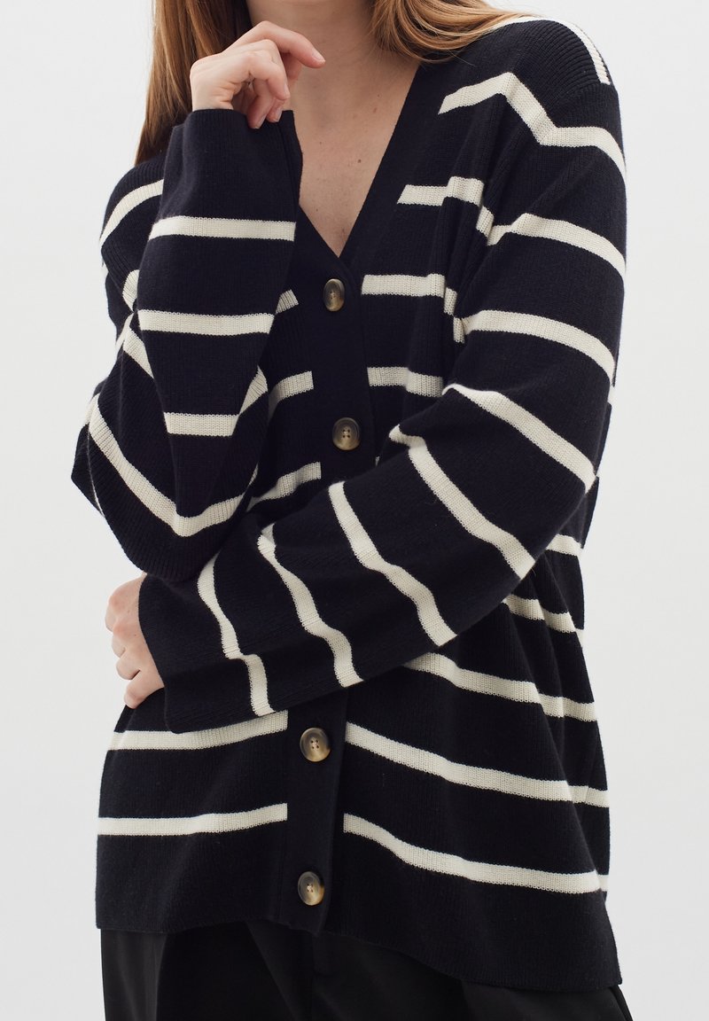 Námořnický a bílý pruhovaný cardigan s V-výstřihem, velkými zlatými knoflíky a žebrovanou strukturou na rukávech a lemu. Měkký pletený materiál.