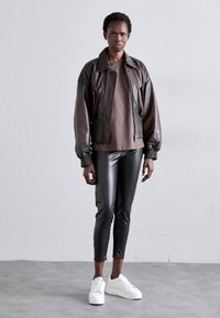 Brun skinnbombarjacka med quiltade detaljer, kombinerad med figurnära svarta fusksskinnbyxor och vita sneakers. Enkel design, utan mönster.