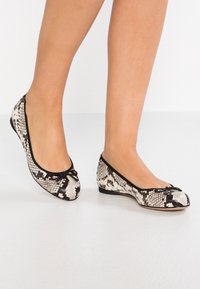 Ballet flats with a black and white snake print pattern, featuring a rounded toe and a delicate bow accent. Low-profile, flexible sole.