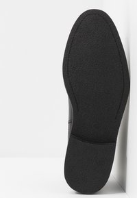 Zapato negro con suela de goma texturizada, parte superior lisa y punta redondeada. Lateral con ligera curva y tamaño marcado como 42.