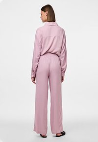 Chemise rose clair à manches longues avec col, associée à un pantalon large assorti. Tissu doux, coupe décontractée et détails de taille élastique.