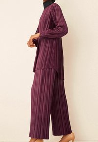 Ensemble deux pièces plissé en violet profond avec des rayures verticales. Le haut est à manches longues avec des détails de bouton, et le pantalon est à jambe large.