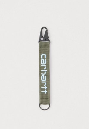 Prívesok na kľúče z olivovo zelenej látky s čiernou sponou a strieborným krúžkom, označený nápisom "carhartt" svetlomodrým kurzívnym písmom.