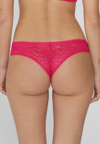 Rosa Spitzen-Tanga mit floralem Muster, gekennzeichnet durch ein niedrig geschnittenes Design und gewellte Kanten. Die Rückseite zeigt eine glatte, enganliegende Form.