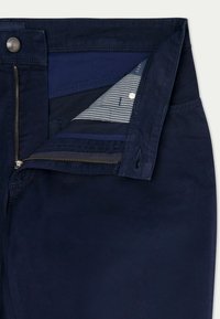 Marineblaue Hose mit Reißverschluss, ausgestattet mit einem gestreiften Taschenfutter. Glatte Textur mit Metallbeschlägen und farblichen Akzenten im Inneren.