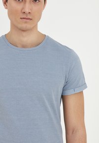 Svetlomodré tričko s okrúhlym výstrihom a krátkymi rolled rukávmi. Tkanina má jemnú textúru a priliehavý strih. Žiadne viditeľné vzory ani akcenty.