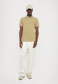 Polo shirt tan, pantaloni wide-leg crem, și pantofi bej. Capac asortat tan cu logo. Design simplu, material din bumbac, detalii minime.