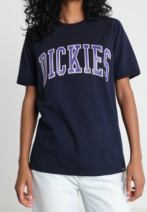 Granatowy bawełniany t-shirt z krótkimi rękawami, z dużym fioletowym napisem "DICKIES" na piersi. Na dole znajduje się mała metka producenta.