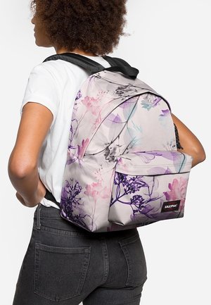 Person mit einem Rucksack mit Blumenmuster in Pink, Lila und Blau, schwarzen Trägern und einem vorderen Eastpak-Logo-Patch.