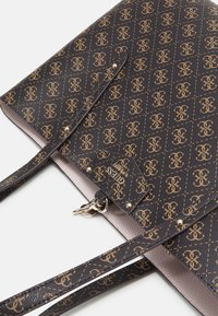 Sac fourre-tout noir texturé avec un motif de logo doré, des fines anses doubles et des accents en métal doré. Intérieur de couleur claire.