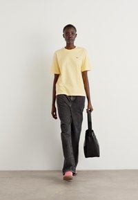 Gul bomull T-skjorte, grå denim jeans, rosa sneakers og en svart totebag. Enkelt design med en avslappet passform og ingen synlige mønstre.