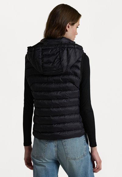 Vesta puf din material negru, cu glugă, având un design matlasat, textură netedă și o siluetă ajustată, purtată peste un top din material negru cu mânecă lungă.