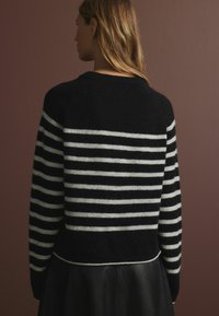 Schwarz-weiß gestreifter Pullover mit flauschiger Textur, rundem Ausschnitt und lockerer Passform, kombiniert mit einem schwarzen Lederrock, von hinten betrachtet.