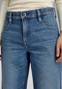 Ljust blå denimjeans med hög midja, rak bendesign, fem fickor och en silverknapp. Mjuk textur med urtvättade områden.