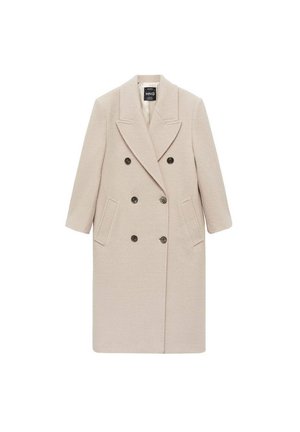 Persona que lleva un abrigo cruzado de lana beige, suéter de canalé crema, camisa blanca con cuello y un cinturón negro fino en la cintura.