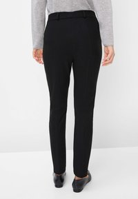 Pantalons noirs ajustés avec une texture lisse, présentant une coupe droite et des détails de couture visibles. Portés avec des chaussures noires.