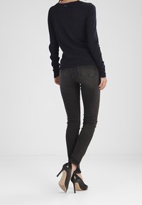 Mörk marinblå långärmad topp i kombination med åtsittande mörka jeans och svarta högklackade skor, med en slät textur och skräddarsydd design.