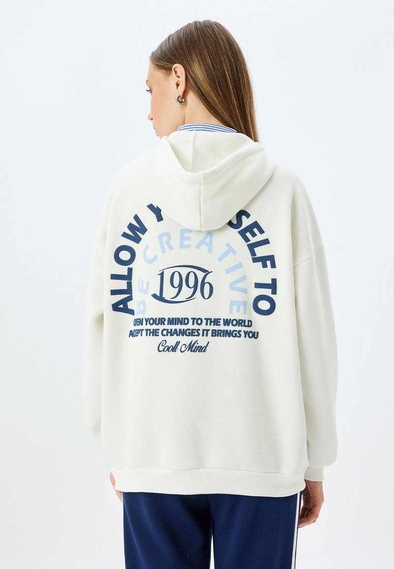 Felpa con cappuccio color crema realizzata in tessuto morbido, con grande testo blu navy sulla schiena, che riporta "1996" e frasi motivazionali.