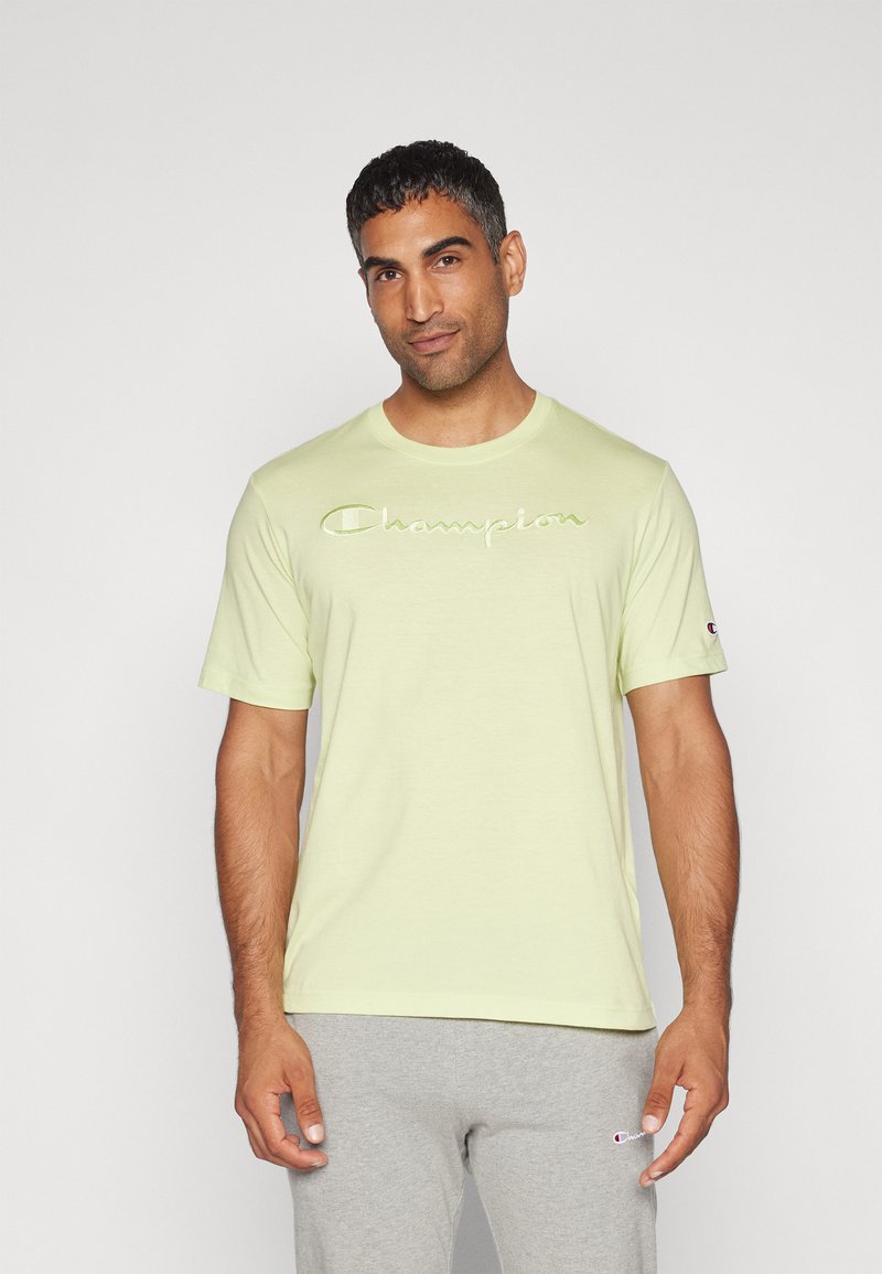 Hellgelbes T-Shirt mit kurzen Ärmeln und embossed "Champion"-Logo, kombiniert mit grauen Sweatpants mit kleinem Logo.