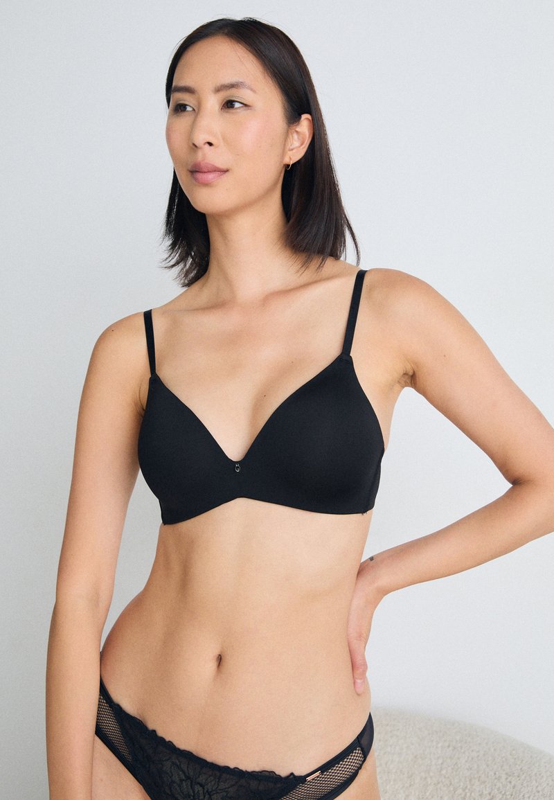 Schwarzer, nahtloser BH mit verstellbaren Trägern, V-förmigen Cups und einer kleinen zentralen Verzierung. Glatte Textur, minimalistisches Design, vielseitiger Stil.