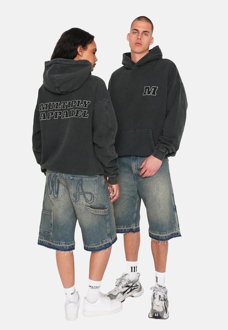 Tmavě šedá mikina s kapucí s nápisem "MULTIPLY APPAREL" na zádech, doplněná o vybledlé modré denimové šortky s dekoračním prošitím a kapsami.