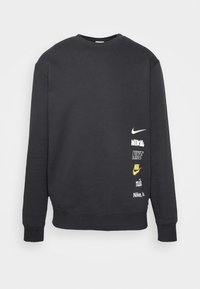 Sudadera negra de manga larga con cuello redondo, con varios logos de Nike en blanco y amarillo apilados verticalmente en la parte inferior derecha.
