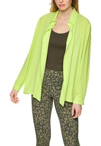 Neon green lightweight button-up shirt with long sleeves worn over a brown tank top and patterned olive green leggings featuring a leopard print.