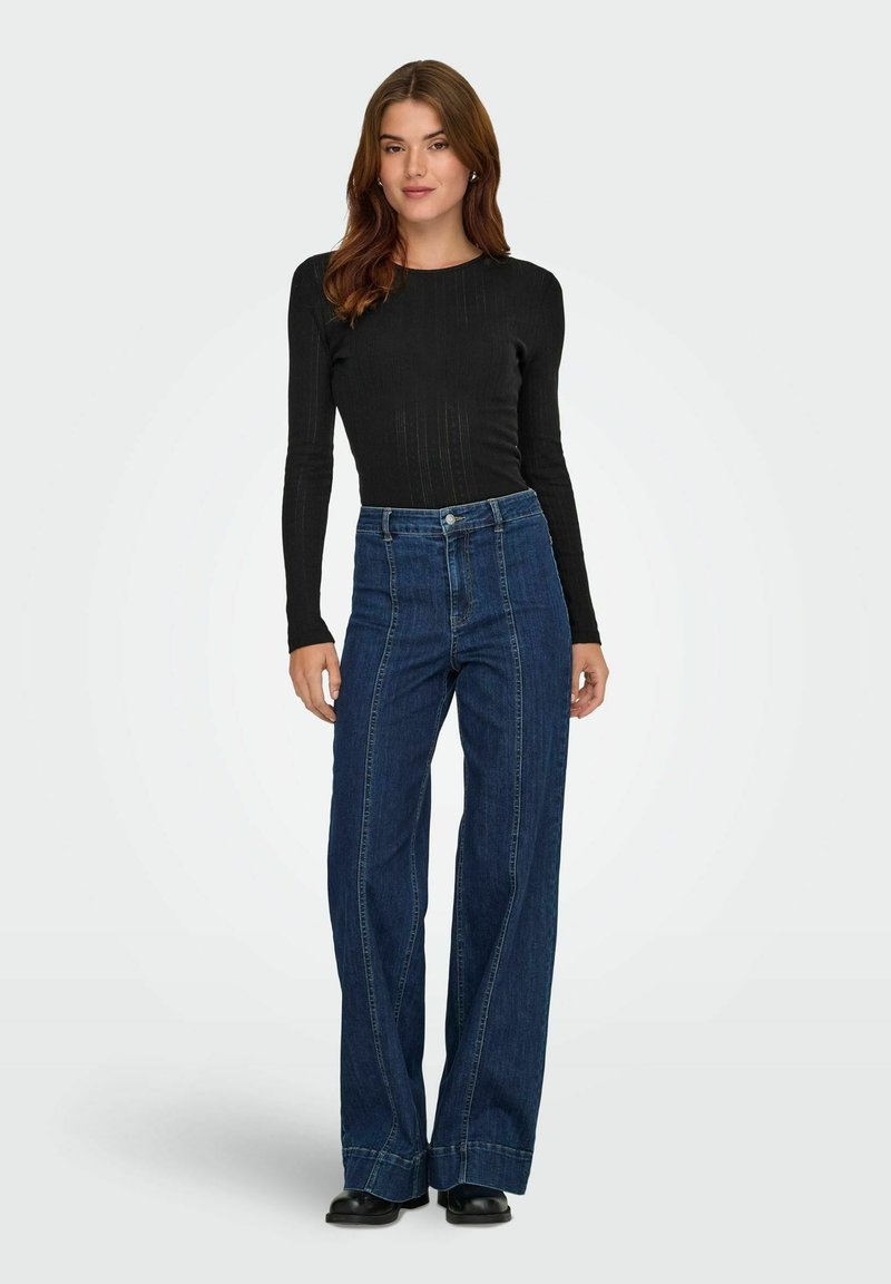 Svart ribbad långärmad topp i kombination med högmidjade, vida blå denimjeans som har kontrasterande sömmar och rå fåll.