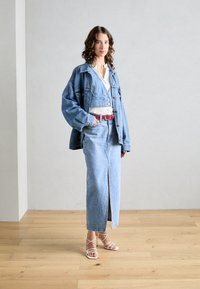 Setti denim-maiset jakke ja hame vaaleansinisinä, valkoisen paidan ja punaisen vyön kanssa. Hiekanväriset sandaalit täydentävät ilmeen.