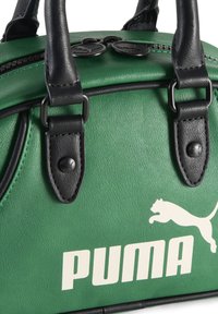 Sac à main synthétique vert avec des accents en cuir noir, anses supérieures et quincaillerie en argent. Présente un logo Puma blanc bien visible et une surface texturée.