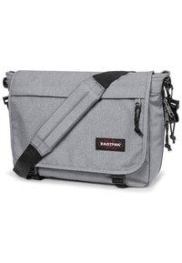Borsa a tracolla grigia realizzata in tessuto resistente, con una patta anteriore, una tracolla regolabile e il logo Eastpak sul davanti. Numerosi scomparti con zip.