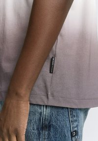 Grijs-verloop kortemouwen overhemd met een gladde textuur, voorzien van een label aan de zijkant en versleten blauwe spijkerbroek met zichtbare stiksels.