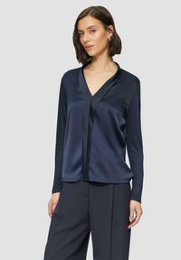 Navy satijnen blouse met lange mouwen en V-hals, voorzien van een contrasterend voorpaneel, met een gladde textuur en een relaxed fit, gecombineerd met donkere broeken.