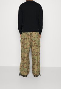Sudadera negra con puños y dobladillo acanalados, combinada con pantalones cargo de camuflaje verde que cuentan con múltiples bolsillos y dobladillos ajustables.