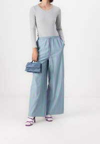Gray long-sleeve ribbed top paired with wide-leg pants featuring vertical green and purple stripes. Small blue handbag and purple-heeled sandals.