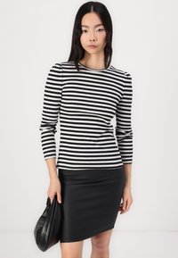 Fekete-fehér csíkos bordázott hosszú ujjú felső, testhez simuló szabásban, fekete bőr mini szoknyával és egy puha fekete clutch-táskával párosítva.