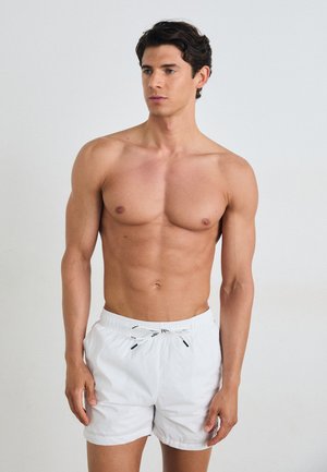 Shorts de bain blancs avec une taille élastique et un cordon noir, présentant une texture lisse et une coupe décontractée. Aucun motif ni élément métallique visible.