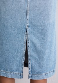 Lichtblauwe denim rok met een split aan de voorkant, zichtbare stiksels en een zoom die aan de onderrand iets is uitgerafeld.