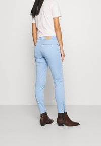 Ljusblåa skinny jeans med en slät textur, utrustade med dragkedjor vid anklarna, bakfickor och en beige logotypplatta på midjan.