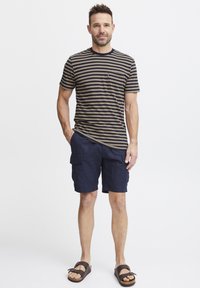 Gestreiftes, dunkelbeiges und marineblaues T-Shirt mit Rundhalsausschnitt, kombiniert mit marineblauen Cargo-Shorts mit Taschen und braunen Sandalen mit verstellbaren Riemen.