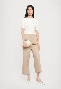 Top bianco a righe a maniche corte, pantaloni larghi beige, borsa crema e mules a punta di una tonalità chiara su uno sfondo neutro.